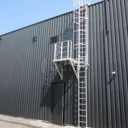 Plataforma con balcón de acceso y entrada lateral a una escalera con jaula y cubierta de metal usada para llegar a la puerta de primer piso en una fábrica.  