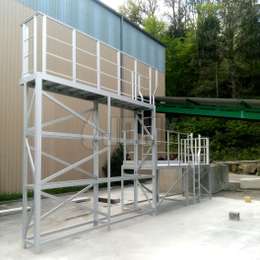 Plataforma de acceso fija con dos niveles, escaleras fijas y barandillas, utilizada para acceder a remolques y cargas de camiones.